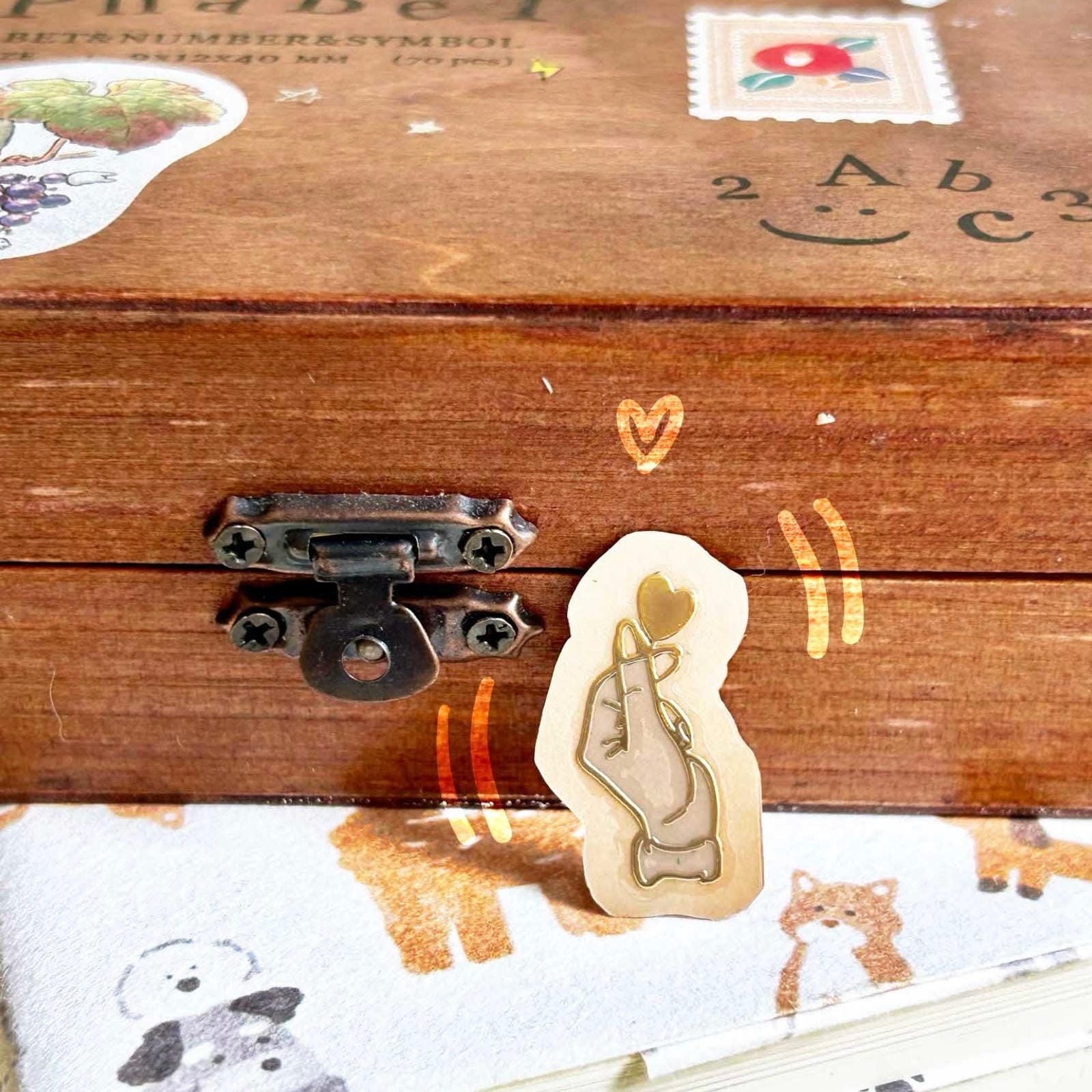 Small metallic Gold transfer sticker of a finger heart gesture with a raised 3D finish on a laptop