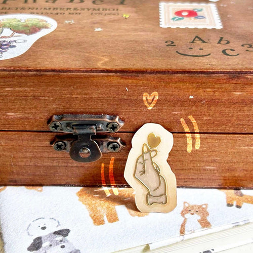 Small metallic Gold transfer sticker of a finger heart gesture with a raised 3D finish on a laptop