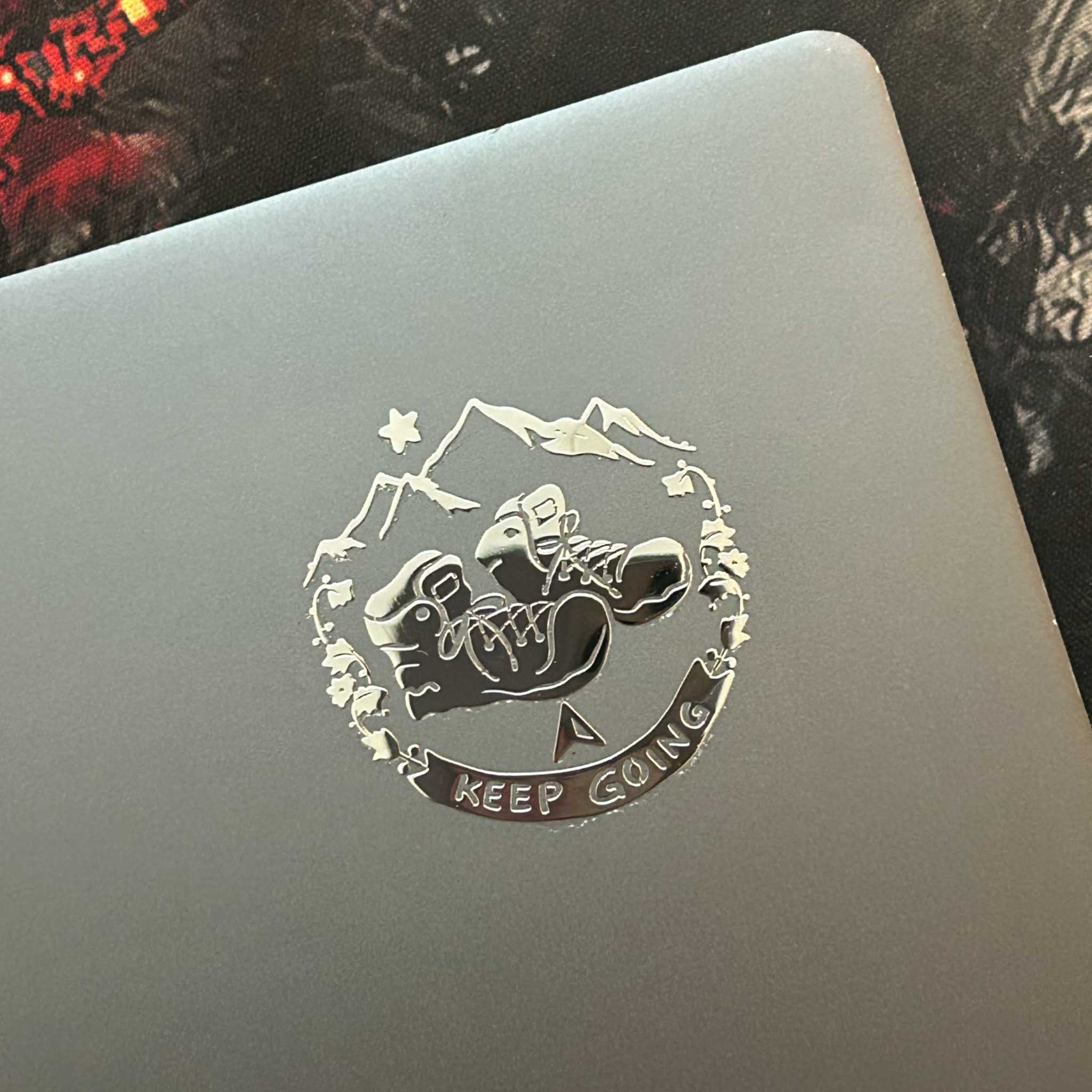 A premium silver metallic Travel sticker featuring cozy hiking boots and mountains. Raised 3D texture, waterproof, and perfect for wanderers. 