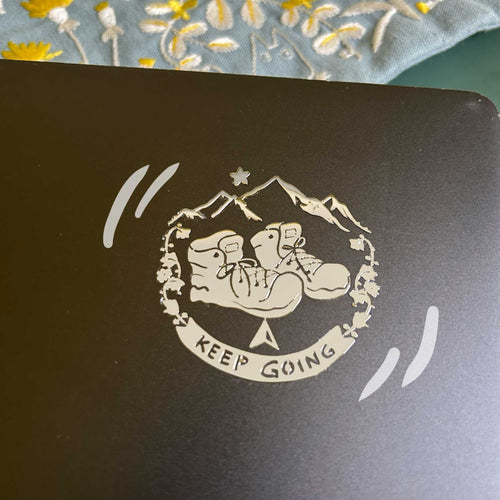 A premium silver metallic Travel sticker featuring cozy hiking boots and mountains. Raised 3D texture, waterproof, and perfect for wanderers. 