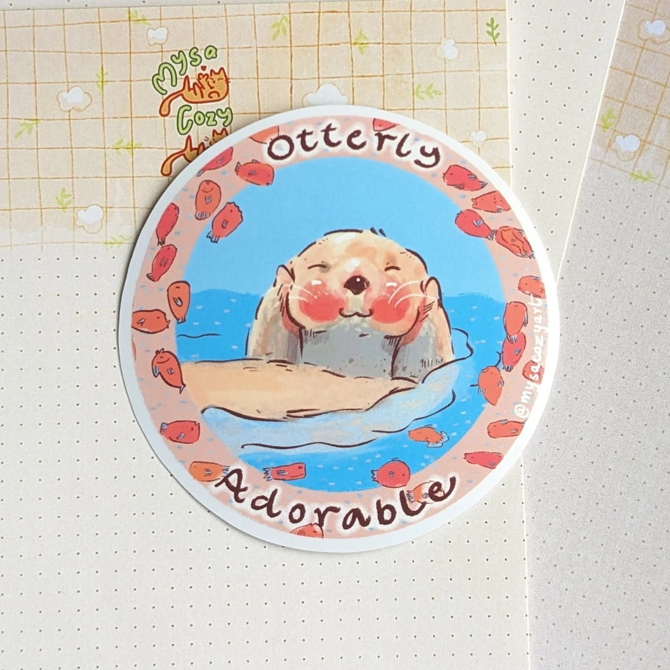 Hand-drawn illustration of a cute otter with the punny text 'Otterly Adorable' on a matte die-cut sticker.
