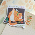 Funny sticker of a cat sitting on a laptop keyboard with the text 'Powered by Assholes' in a playful font.