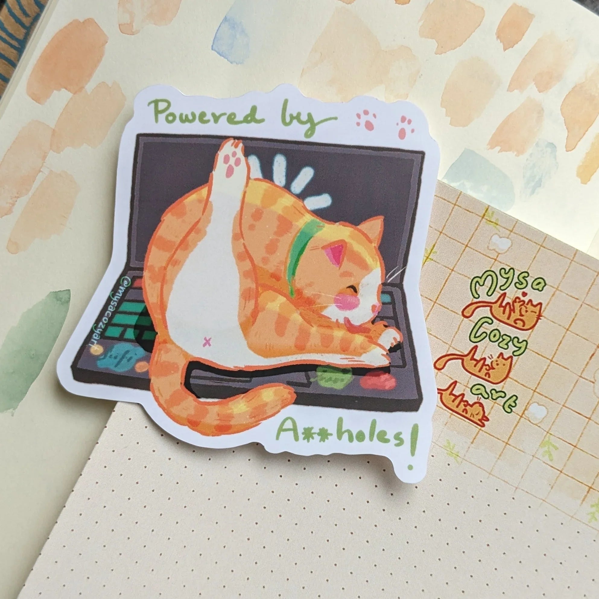 Funny sticker of a cat sitting on a laptop keyboard with the text 'Powered by Assholes' in a playful font.