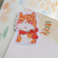 A stylish cat wearing gold earrings and thick-rimmed glasses, illustrated in a cozy matte vinyl sticker style.
